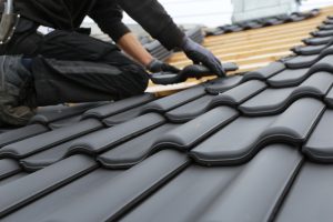Ein Handwerker befestigt Dachziegel auf einem Dach, während er die AluProfile für eine Photovoltaik-Anlage vorbereitet.